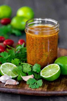 a wooden cutting board topped with cilantro and limes next to a jar of salsa