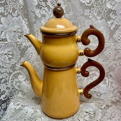 a yellow ceramic teapot sitting on top of a lace covered tablecloth next to a wooden spoon