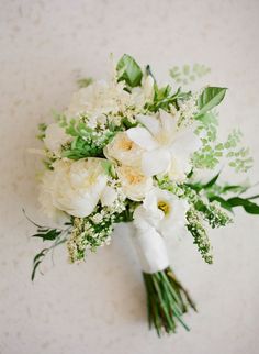 a bridal bouquet with white flowers and greenery on a tableclothed surface