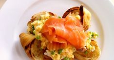 a white plate topped with an egg salad and bagel roll covered in smoked salmon