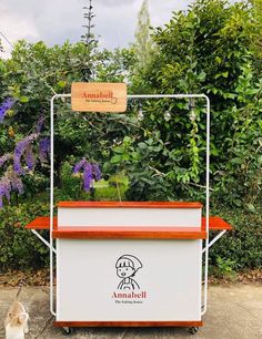 an orange and white food cart sitting in front of some bushes