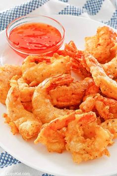 a white plate topped with fried shrimp next to a bowl of sauce on a blue and white checkered table cloth