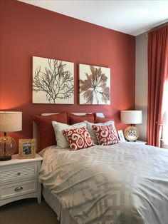 a bedroom with red walls and white bedding, two pictures on the wall above the bed