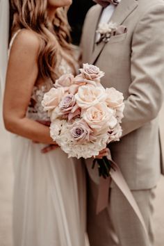 the bride and groom are standing close together in their wedding attire, holding bouquets