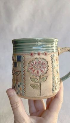 a hand holding a coffee mug with a flower painted on the outside and inside it