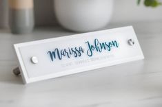 a white name plate sitting on top of a table next to a potted plant