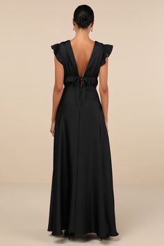 the back of a woman wearing a long black dress with ruffled sleeves and an open neck