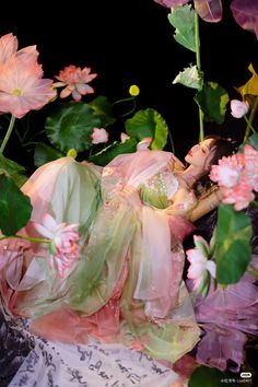 a woman laying on top of a bed of flowers next to green leaves and pink flowers