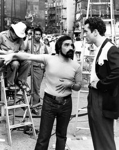 black and white photograph of man with beard standing in front of other men on ladders