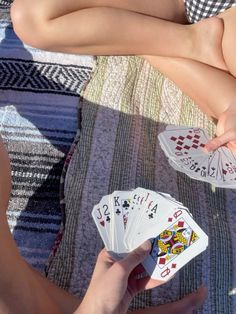 two women are playing cards on a blanket while one woman is holding her leg up