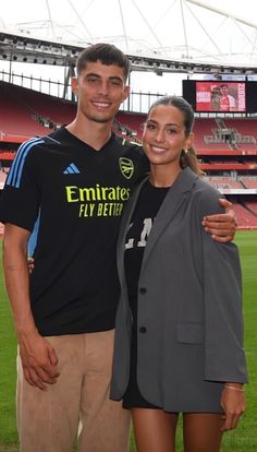 a man and woman standing next to each other in front of a soccer field with fans