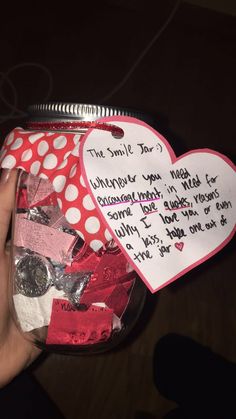 a person holding a jar filled with paper hearts and writing on the label that says i love you