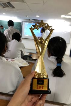 a person is holding up a trophy in front of other people at desks with their backs to the camera