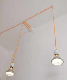 three lights hanging from the ceiling in a room with white walls and orange cords attached to them