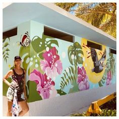 a woman standing in front of a colorful wall with flowers and birds painted on it