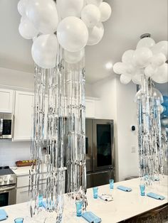 balloons are hanging from the ceiling above a kitchen counter with blue and white napkins on it