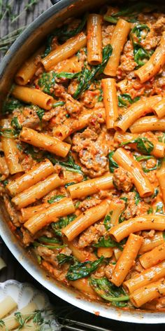 pasta with meat and spinach in a pan on a table next to utensils