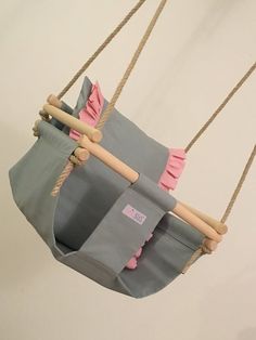 a gray and pink bag hanging from a rope with two wooden sticks sticking out of it