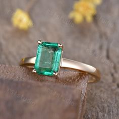 an emerald ring sitting on top of a piece of wood