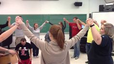 a group of people standing in a room with their hands up to the ceiling and arms raised