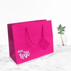 a pink shopping bag next to a small plant on a marble countertop with the words add your logo printed on it