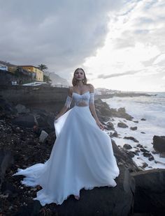 a woman in a wedding dress standing on rocks near the ocean