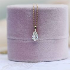 a necklace with a diamond in it on top of a purple velvet box that is sitting on a table