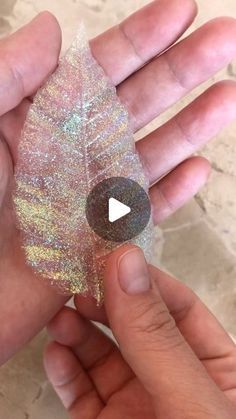 someone is holding a leaf with glitter on it and the other hand is holding an object