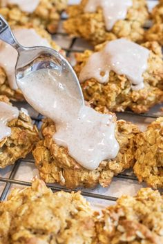 a spoon is being drizzled with white icing on some oatmeal cookies