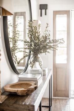 a wooden table topped with a vase filled with green plants next to a large mirror