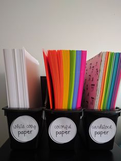 three plastic containers filled with different colored papers on top of a black table next to each other