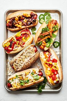 hot dogs with toppings and vegetables on a metal tray, ready to be eaten