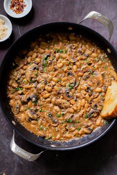 a skillet filled with beans and mushrooms on top of a table next to bread