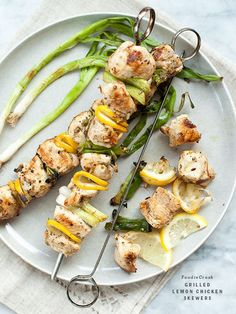 chicken and asparagus skewers on a white plate with lemon wedges