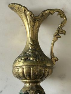 an ornate brass vase with green marbles on the bottom is shown in front of a white wall