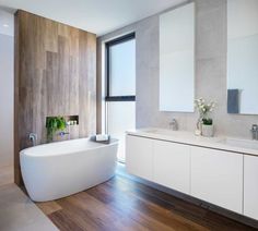 a large white bathtub sitting next to a window in a bathroom with wood flooring