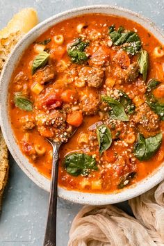 a white bowl filled with pasta and meat soup on top of a blue surface next to bread