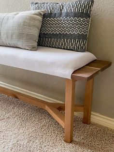 a wooden bench with pillows on it in front of a wall and carpeted floor