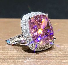 a fancy pink diamond ring sitting on top of a wooden table with diamonds around it