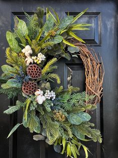 a wreath is hanging on the front door with greenery and pine cones in it