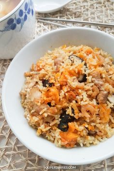 a white bowl filled with rice and meat next to a cup of coffee on a table