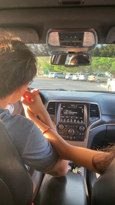 two people sitting in the driver's seat of a car looking at something on the dashboard