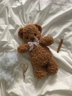 a brown teddy bear laying on top of a bed next to scissors and yarns