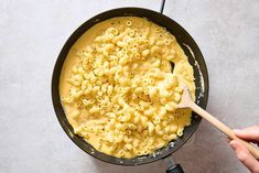 a skillet filled with macaroni and cheese being stirred by a wooden spoon