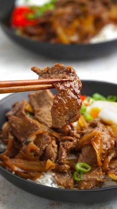 two black bowls filled with meat and vegetables on top of white countertop next to chopsticks