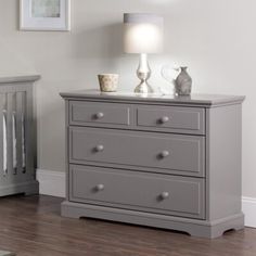 a baby crib next to a dresser with a lamp and pictures on the wall