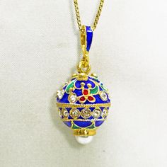 "Miniature egg pendant with tiny red flowers and leaf ornament on the royal blue surface, enameled and 24 K gold plated over solid sterling silver,  designed and made in the tradition and spirit of Faberge jewelry. The pendant is  almost round, with the large imitation pearl at the bottom and a band of clear crystals, separating the top sphere from the bottom one, and a few crystals decorating the upper part of the pendant. The pendant is about 0.8\" ( 18 mm ) without a bail for a chain.   It co Blue Enamel Locket Jewelry, Royal Blue Jewelry For Gift, Royal Blue Jewelry Gift, Royal Blue Jewelry For Gifts, Blue Oval Enamel Necklace, Blue Enamel Oval Pendant Jewelry, Royal Gold Jewelry Gift, Royal Gold Jewelry For Gift, Royal Gold Jewelry As A Gift