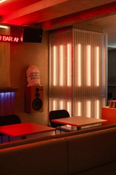 the interior of a bar with red lights and tables in front of it, along with two speakers on the wall