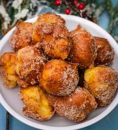 a white bowl filled with powdered sugar covered doughnuts on top of a blue table