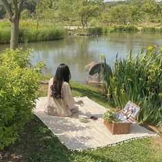 a woman sitting on top of a blanket next to a river with flowers in it